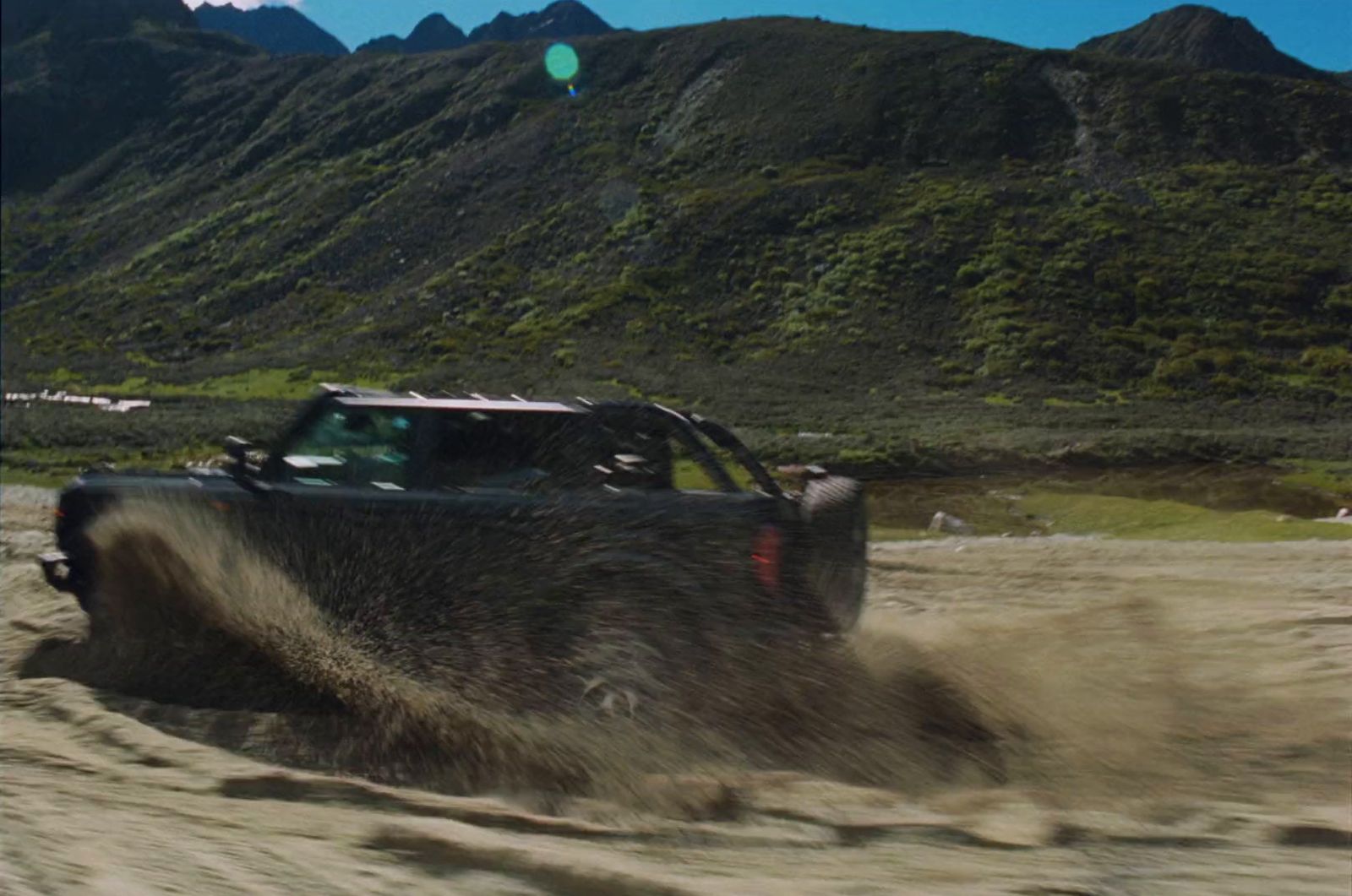 a jeep driving through a sandy area with mountains in the background