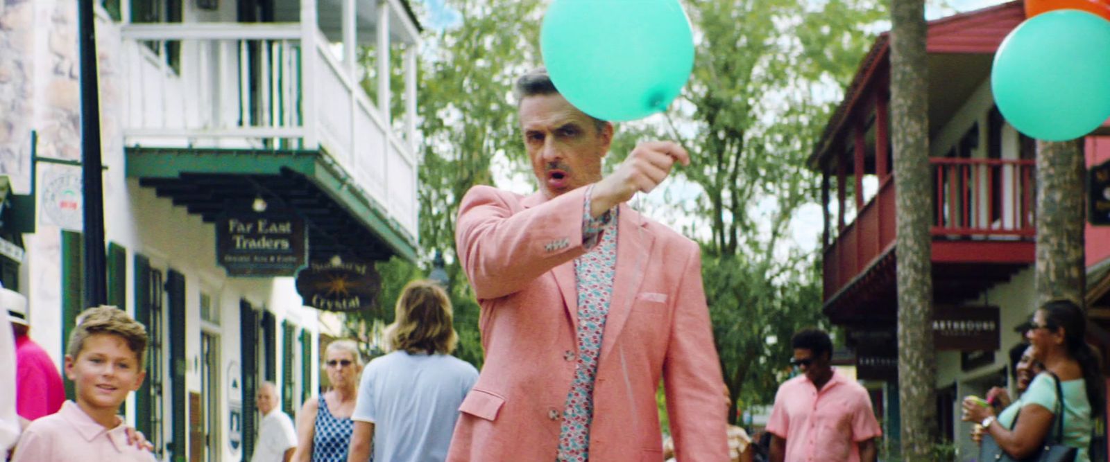 a man in a pink blazer holding green balloons