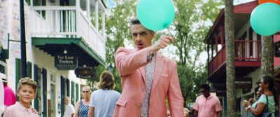 a man in a pink blazer holding green balloons