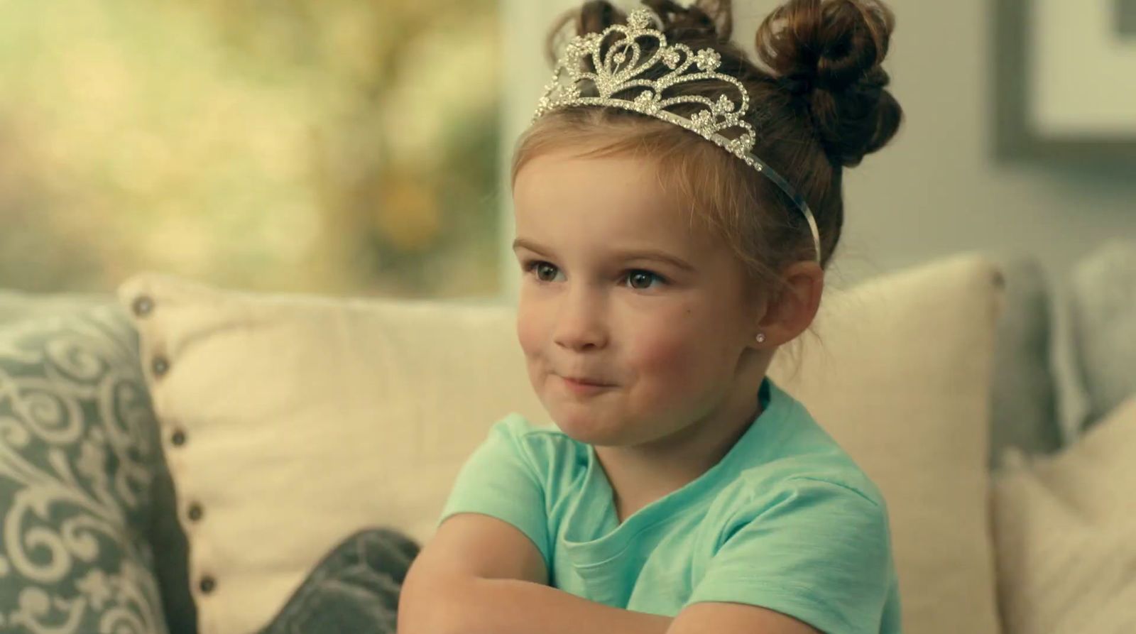 a little girl wearing a tiara sitting on a couch