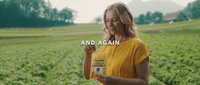 a woman standing in a field holding a bottle