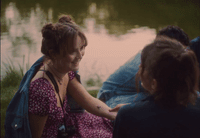 a woman sitting next to a little girl near a body of water