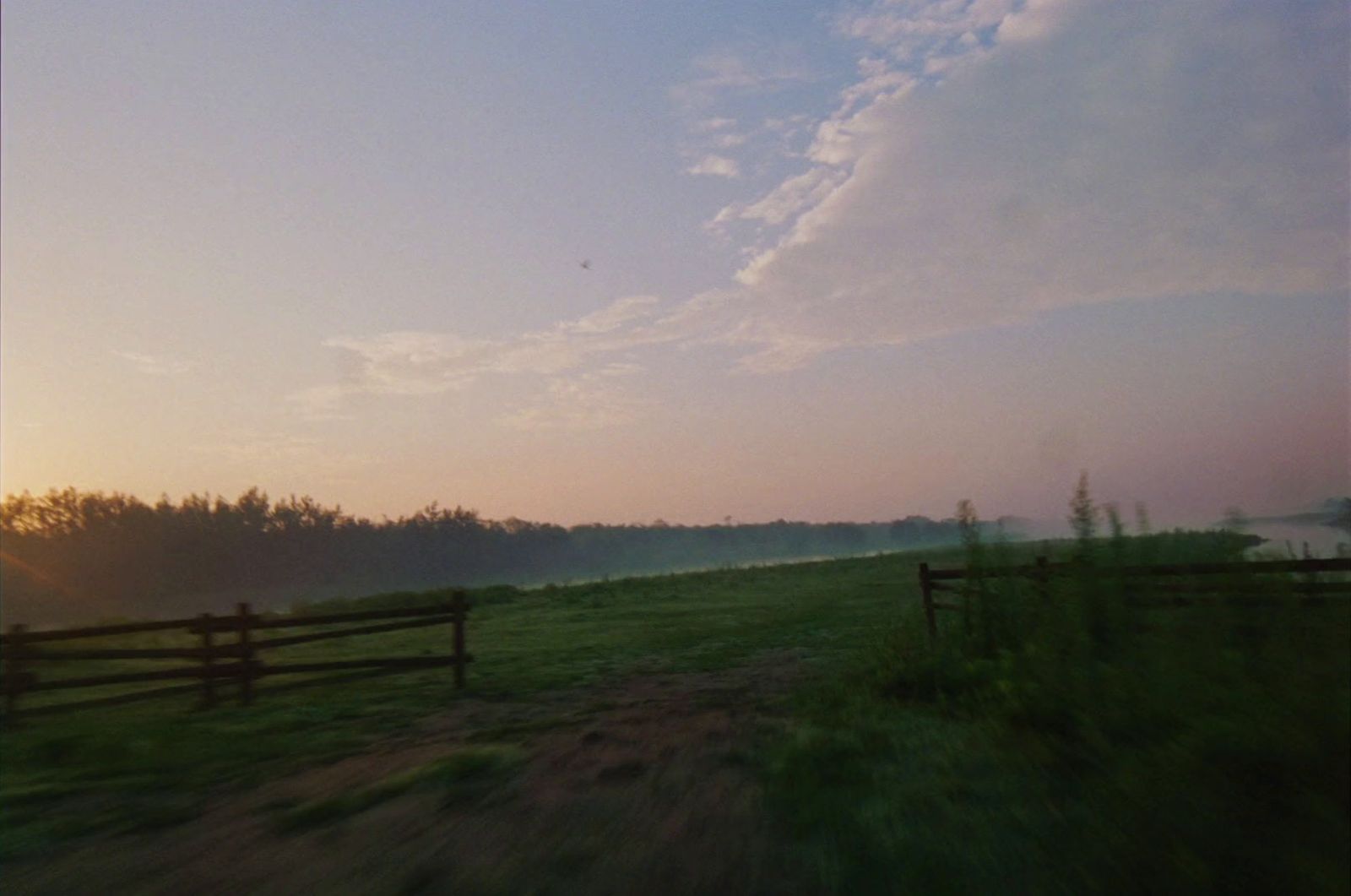 a field with a fence and trees in the background