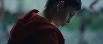 a boy in a red hoodie looking down at his cell phone