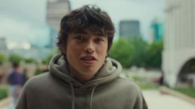 a young man in a hoodie standing on a sidewalk