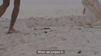 a couple of people walking across a sandy beach