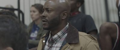 a man in a brown jacket and plaid shirt standing in front of a group of