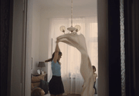 a woman standing in a living room holding a white scarf