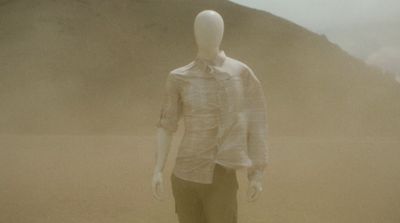 a mannequin wearing a shirt and tie standing in the sand