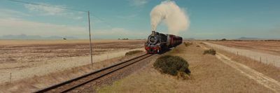 a train traveling down train tracks next to a dry grass field