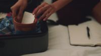 a person putting something in a suitcase on a bed