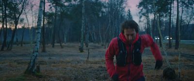 a man in a red jacket walking through a forest