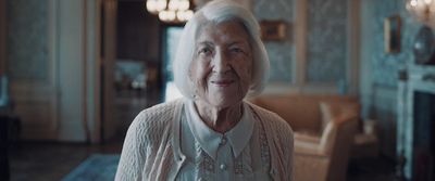 an older woman in a white sweater standing in a living room