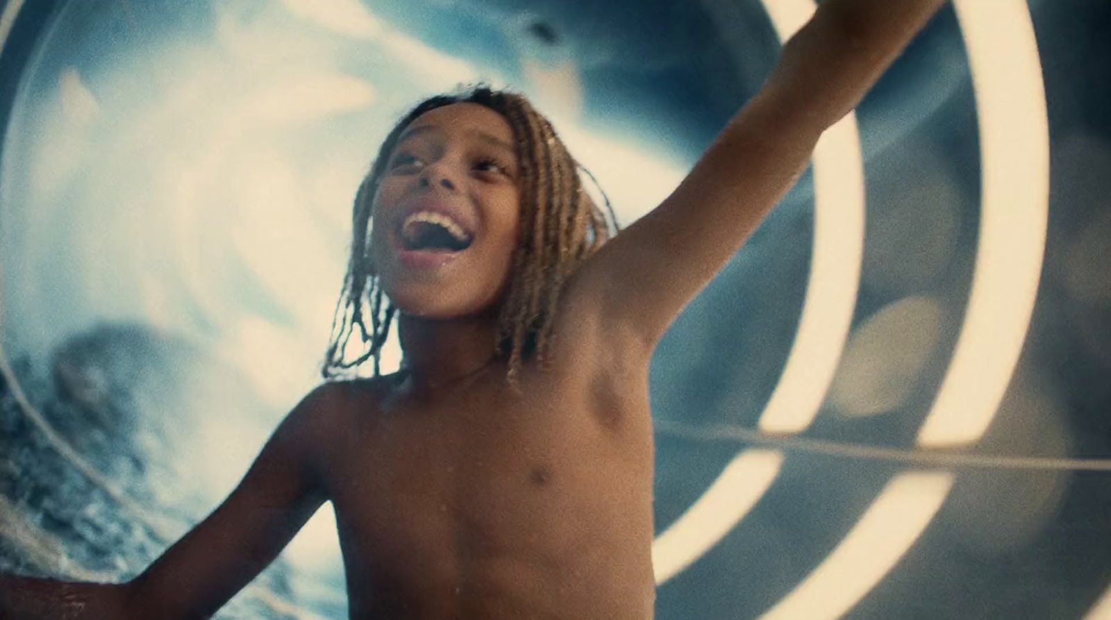 a boy with dreadlocks standing in front of a wall