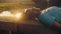 a young boy laying on a ledge next to a river