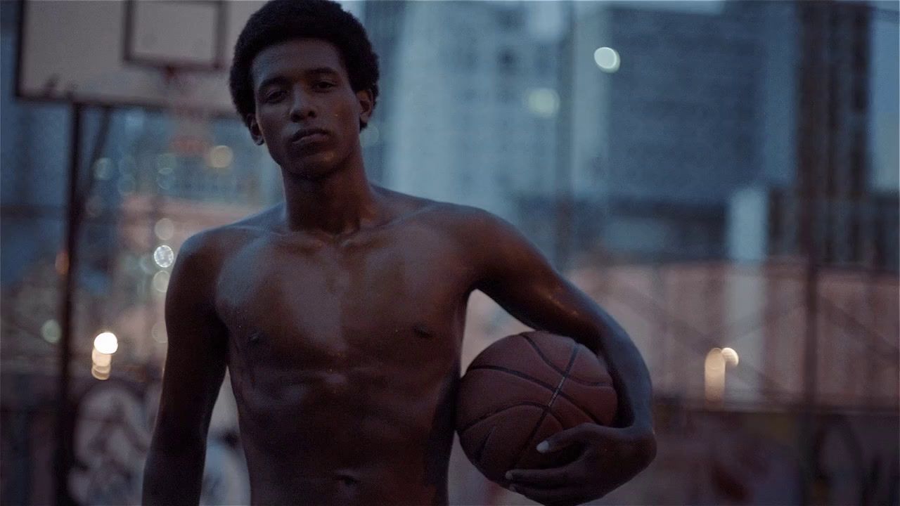 a shirtless man holding a basketball in a city