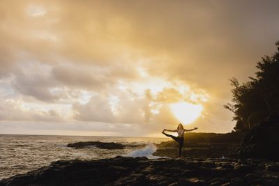 a woman standing on a rocky shore with her arms outstretched