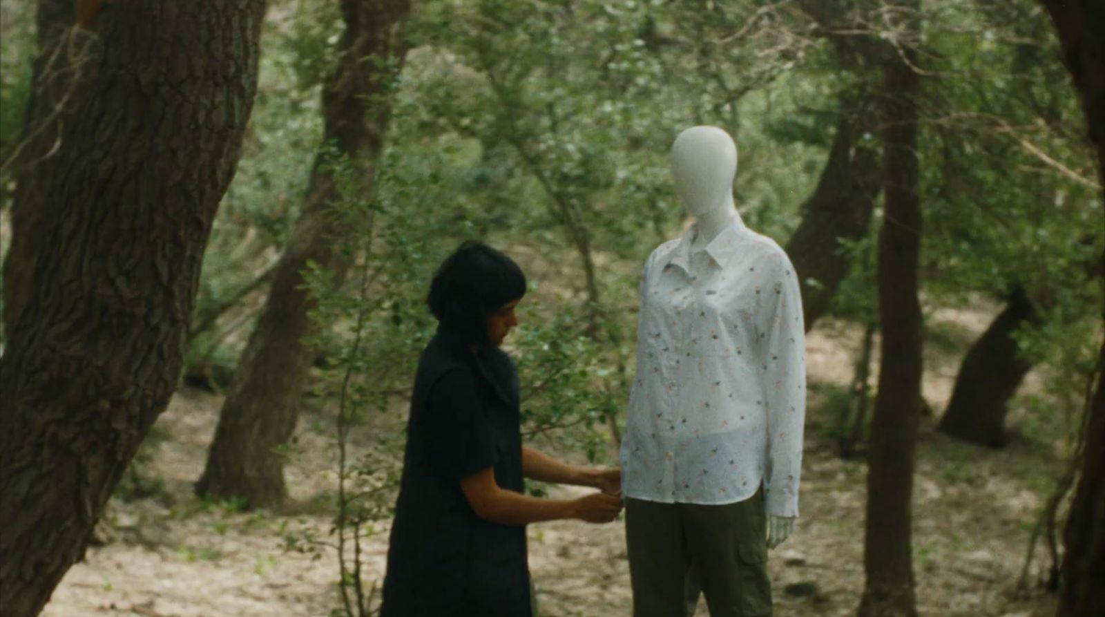 a woman standing next to a mannequin in a forest