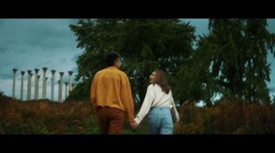 a man and a woman holding hands walking through a field