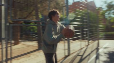 a man holding a basketball standing next to a fence