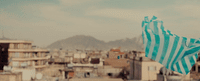 a blue and white striped kite flying over a city