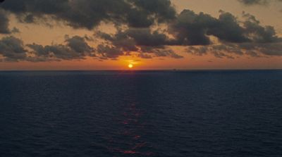 the sun is setting over the ocean on a cloudy day