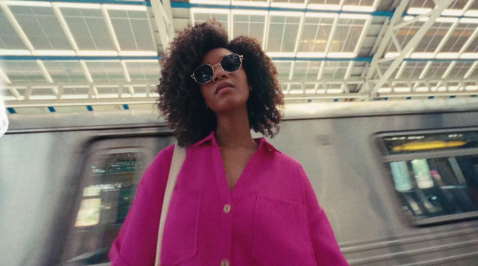 a woman in a pink shirt and sunglasses standing in front of a train