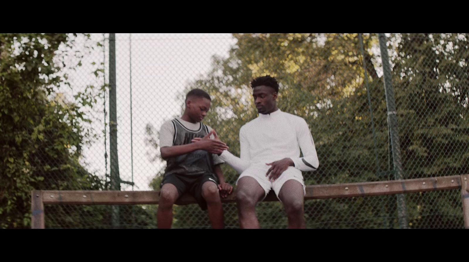 two men sitting on a fence looking at a cell phone