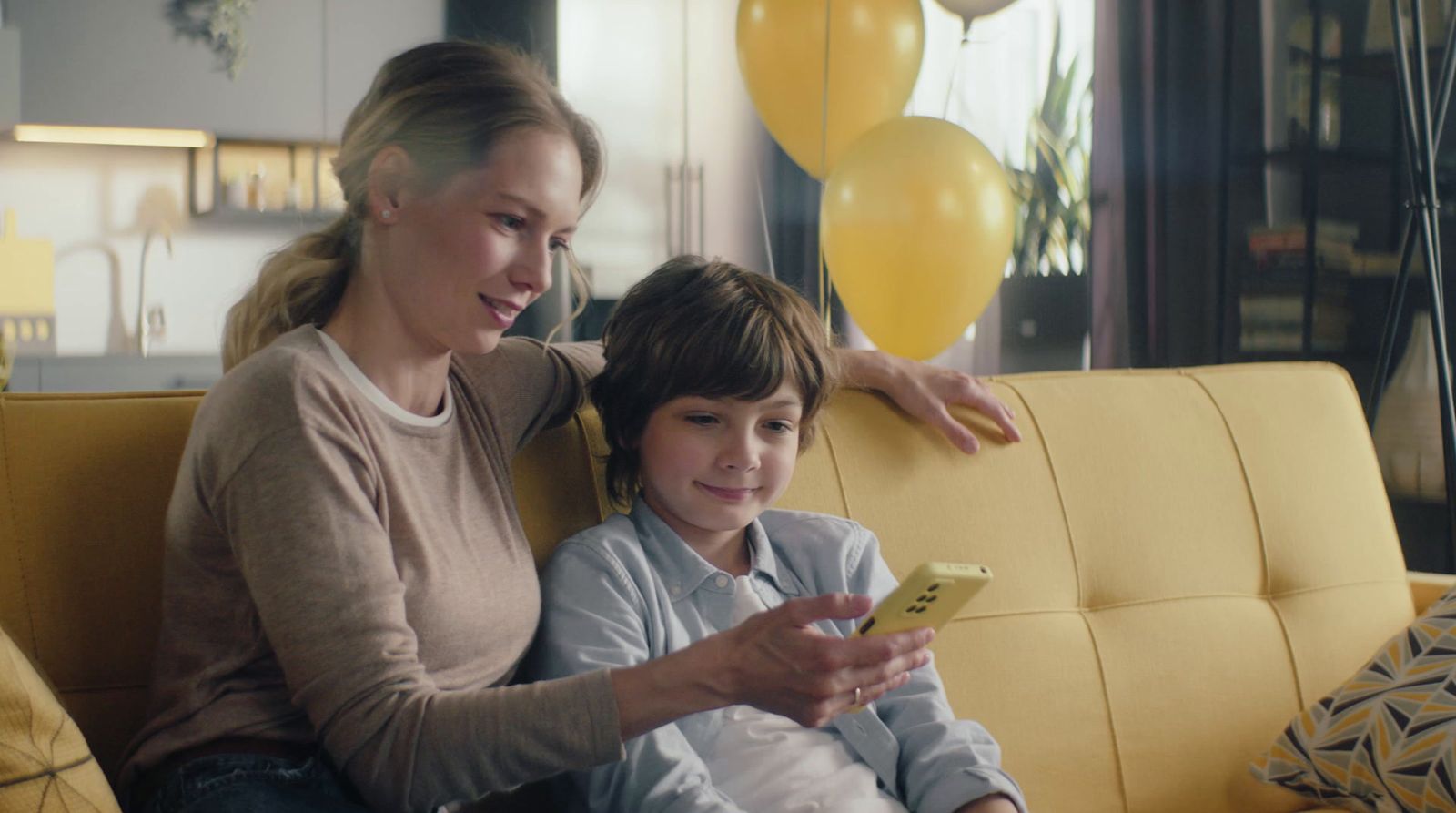 a woman and a boy sitting on a couch looking at a cell phone