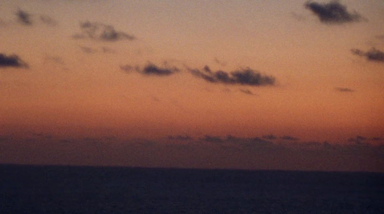 a plane flying over the ocean at sunset