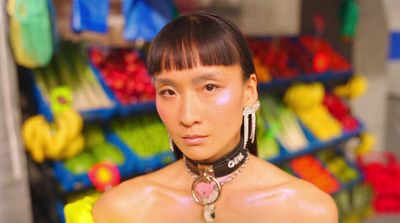 a woman wearing a necklace and earrings standing in front of a fruit stand