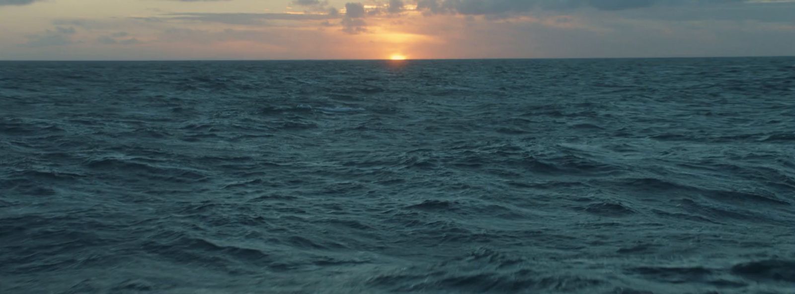 a large body of water with a sun setting in the distance