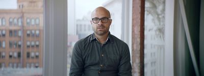 a bald man with glasses sitting in front of a window