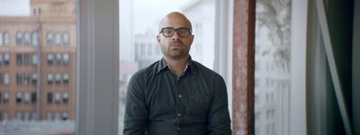 a man with glasses standing in front of a window