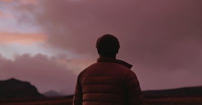 a man standing in a field looking at a cloudy sky