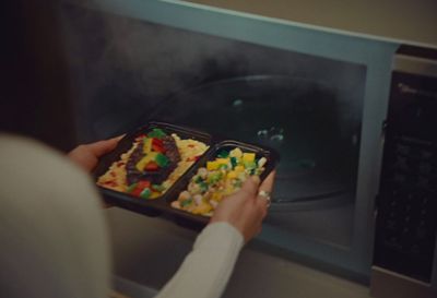 a person holding a tray of food in front of a microwave