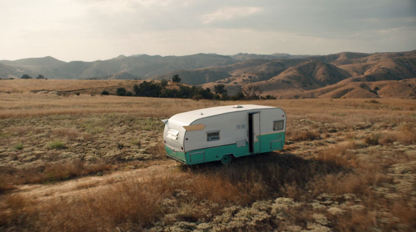 a trailer is parked in a field with mountains in the background