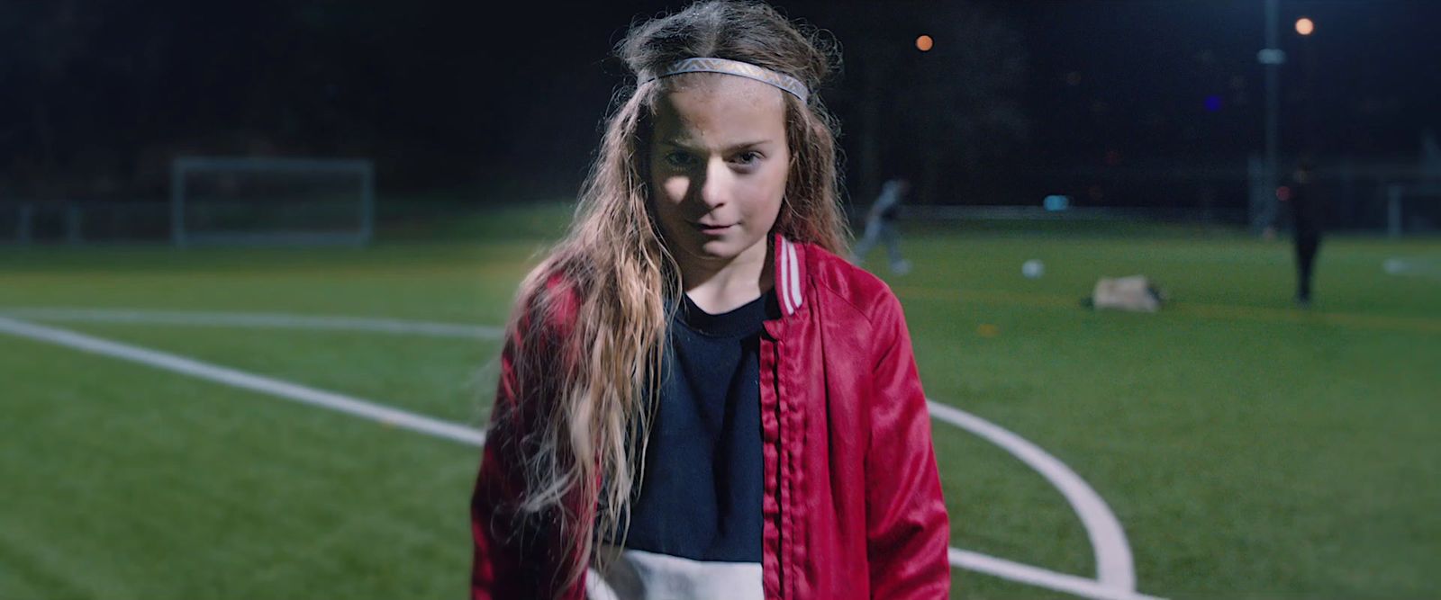 a young girl standing on a soccer field at night