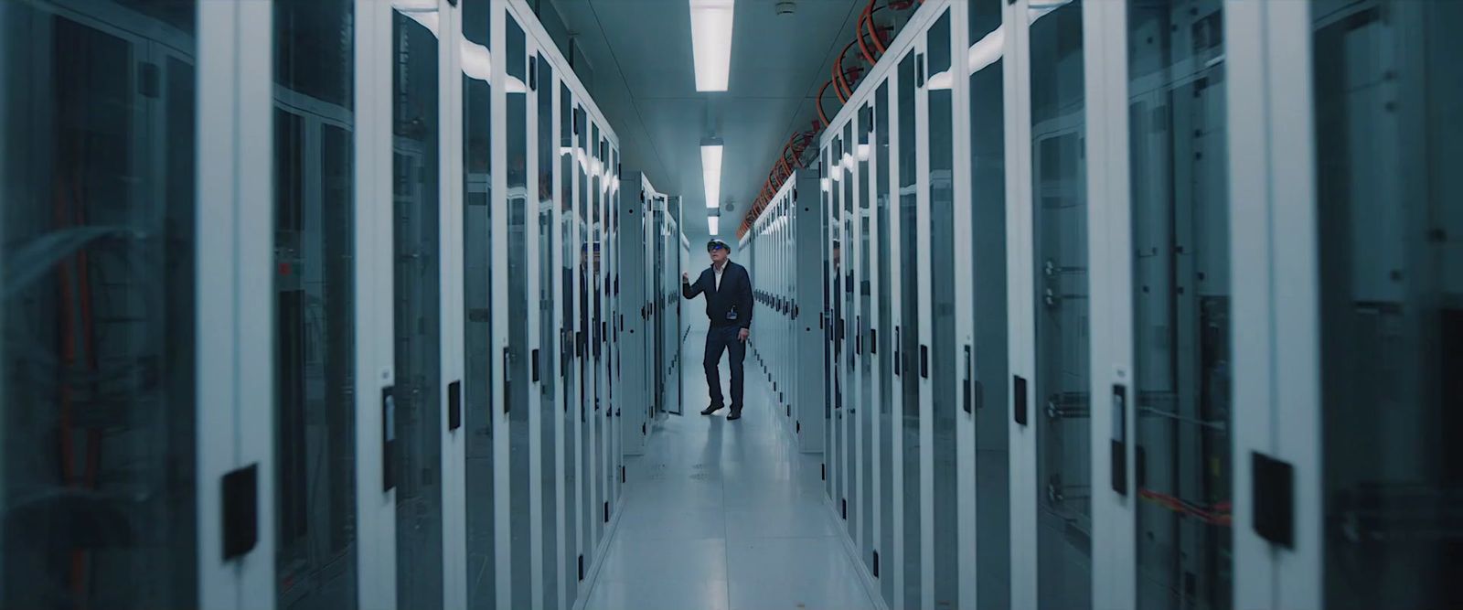 a man walking down a hallway between two rows of servers