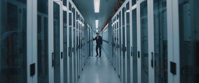 a man walking down a hallway between two rows of servers