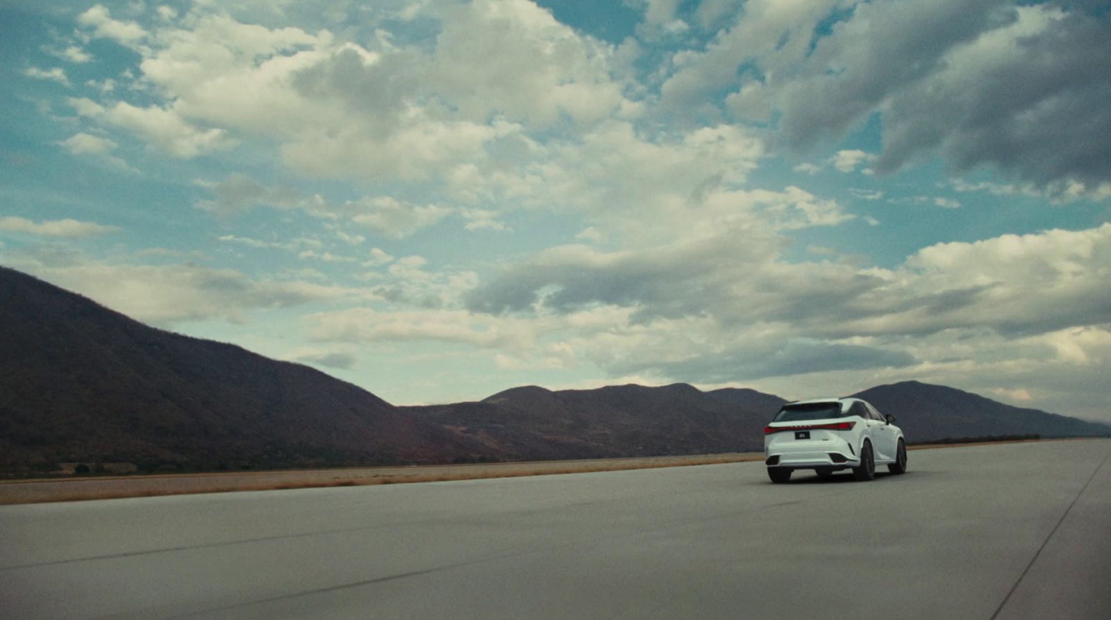 a white car driving down a road with mountains in the background