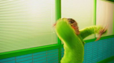 a woman standing in front of a window next to a green wall