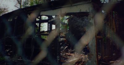 the remains of a building through a chain link fence