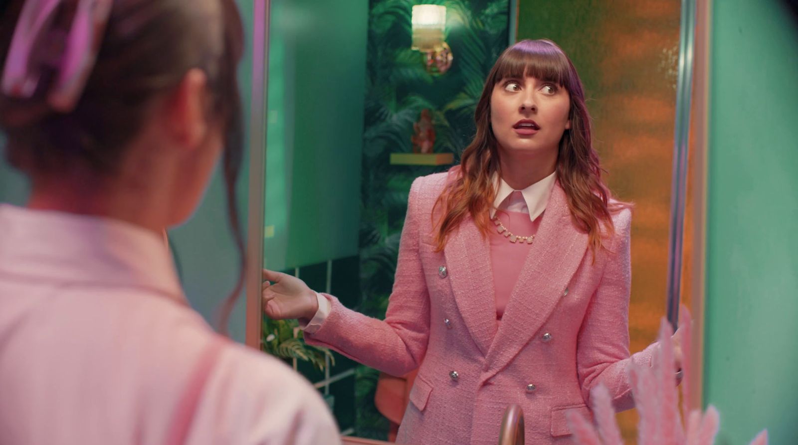 a woman in a pink suit standing in front of a mirror