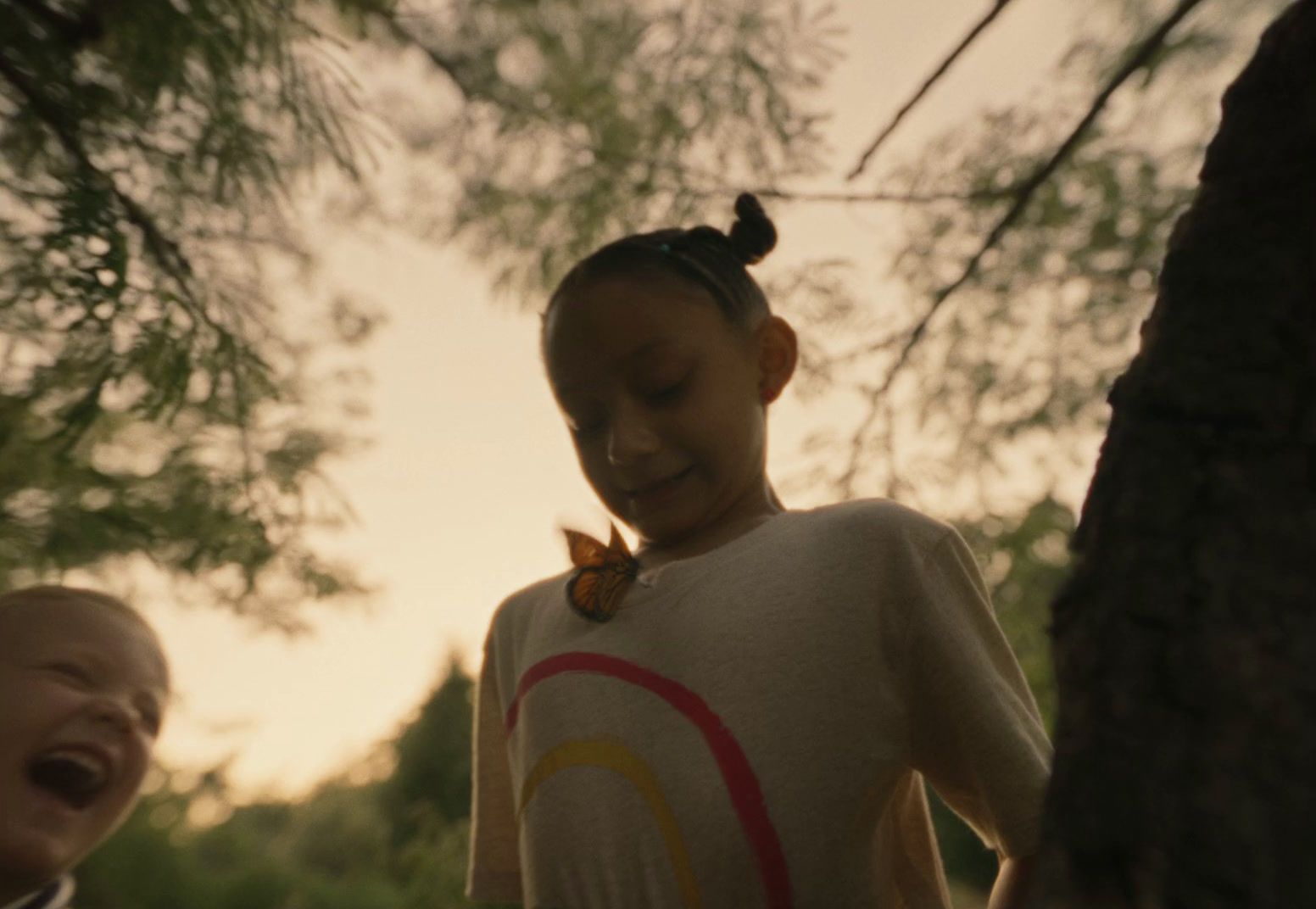 a young girl laughing while standing next to a tree