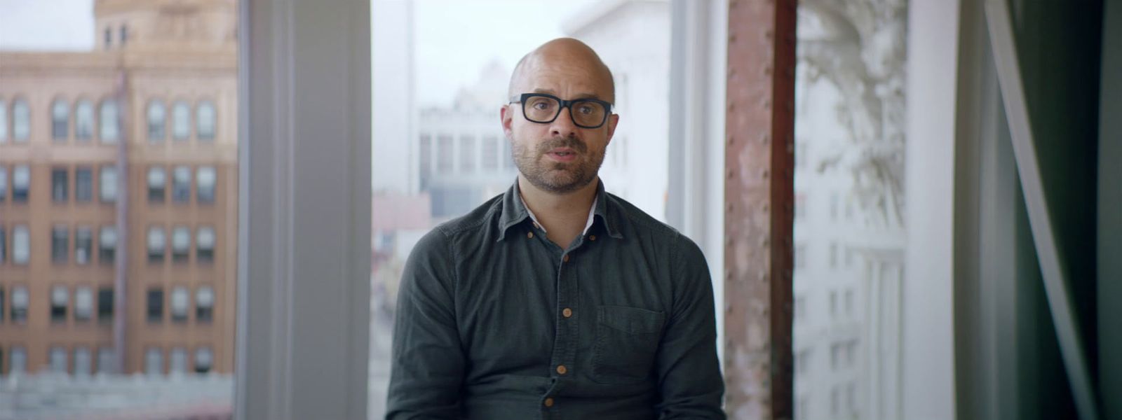 a man with glasses standing in front of a window