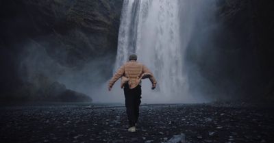 a man walking in front of a waterfall