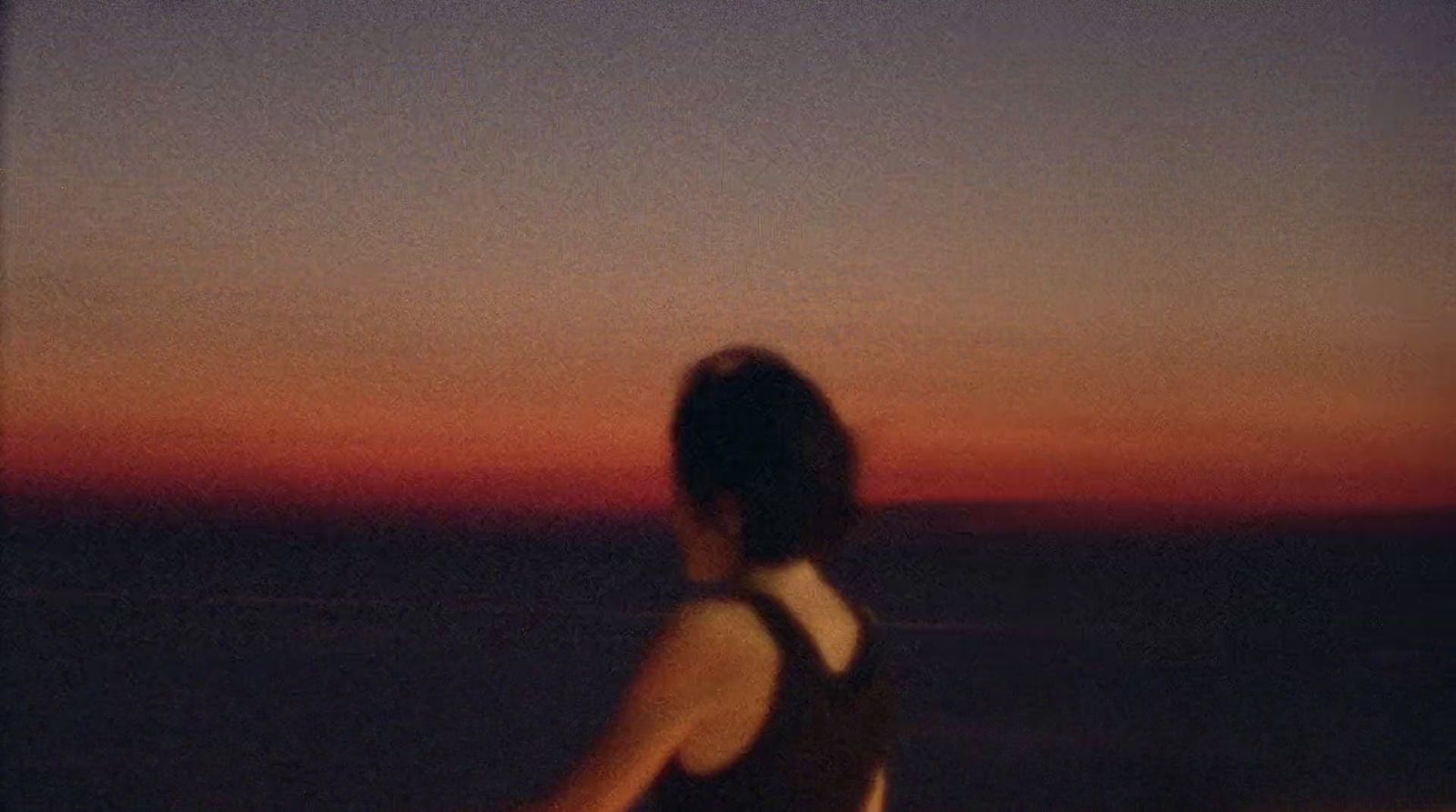 a woman standing in front of the ocean at sunset