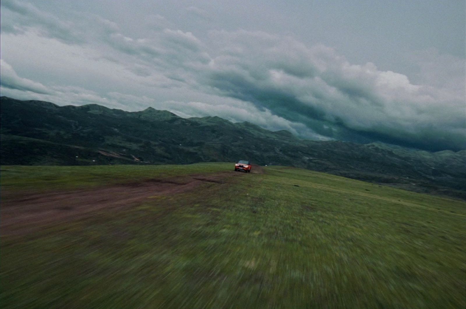 a red truck driving down a lush green hillside