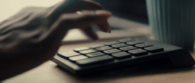 a person typing on a black keyboard next to a cup of coffee